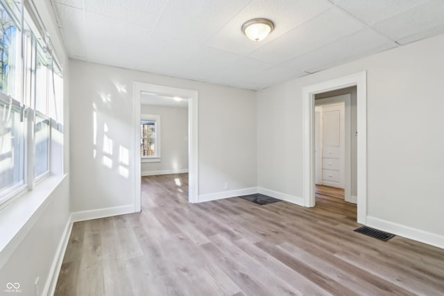 spare room featuring a paneled ceiling, visible vents, baseboards, and wood finished floors