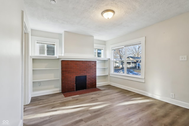 unfurnished living room featuring wood finished floors, a fireplace, baseboards, and a textured ceiling