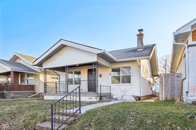 bungalow-style house with covered porch, a chimney, a front yard, and a shingled roof