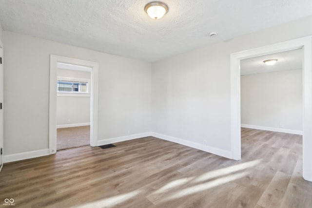 spare room featuring visible vents, a textured ceiling, baseboards, and wood finished floors