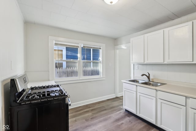 kitchen featuring gas stove, a sink, light countertops, white cabinetry, and light wood-type flooring