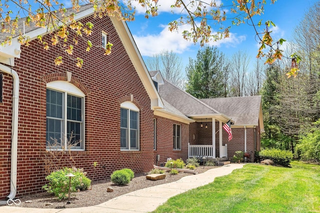 view of front facade featuring a porch, brick siding, roof with shingles, and a front lawn