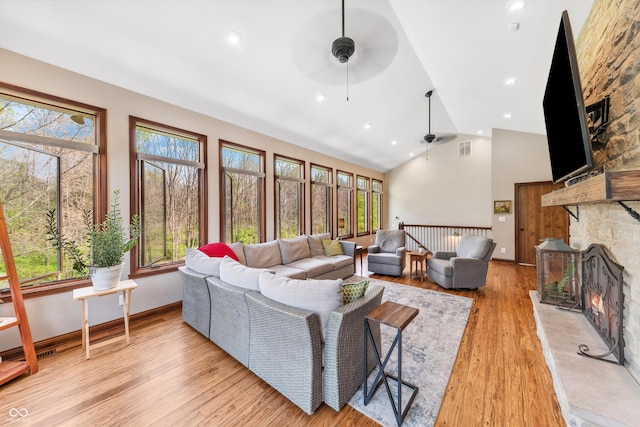 living room with ceiling fan, a stone fireplace, baseboards, light wood-type flooring, and visible vents