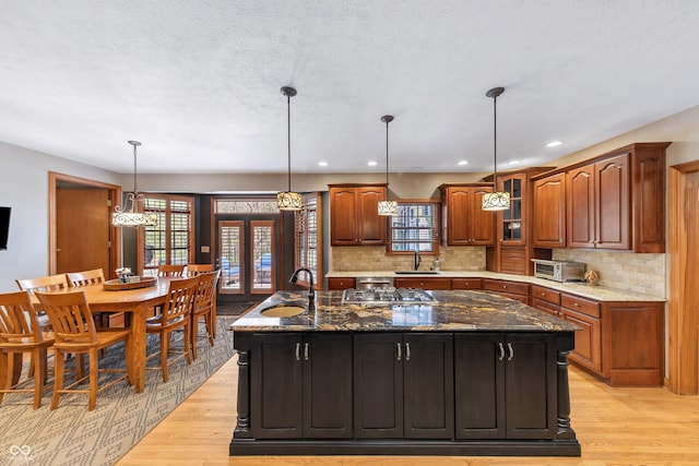 kitchen with a sink, light wood-style flooring, backsplash, and a kitchen island with sink