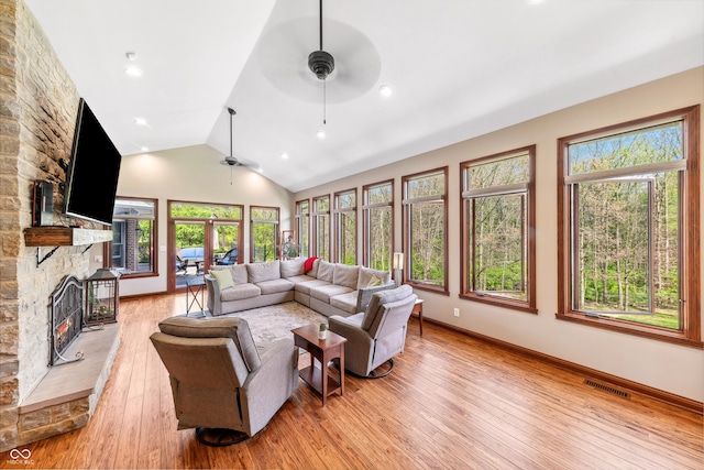 living room with ceiling fan, light wood-style floors, a stone fireplace, lofted ceiling, and visible vents