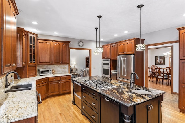 kitchen with a sink, a kitchen island with sink, stainless steel appliances, and light wood-type flooring