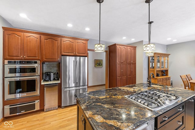 kitchen featuring a sink, light wood-style floors, stainless steel appliances, decorative light fixtures, and a warming drawer