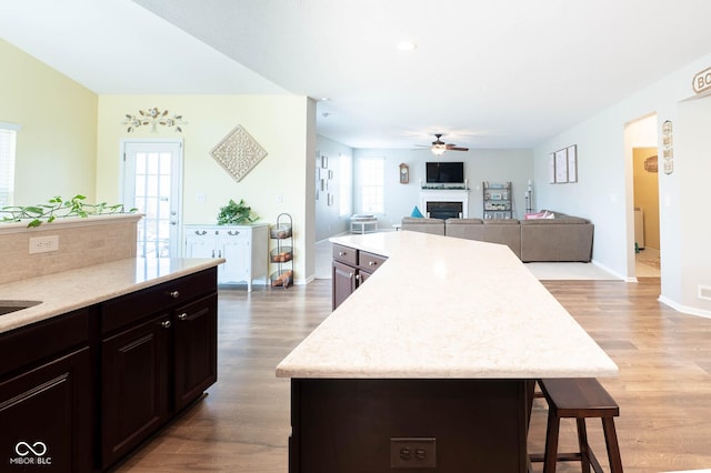 kitchen featuring ceiling fan, open floor plan, a breakfast bar, light wood-type flooring, and a fireplace