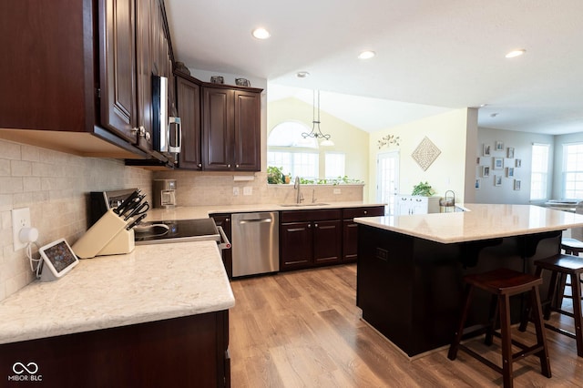 kitchen featuring a kitchen bar, light wood-style flooring, a sink, stainless steel appliances, and dark brown cabinets