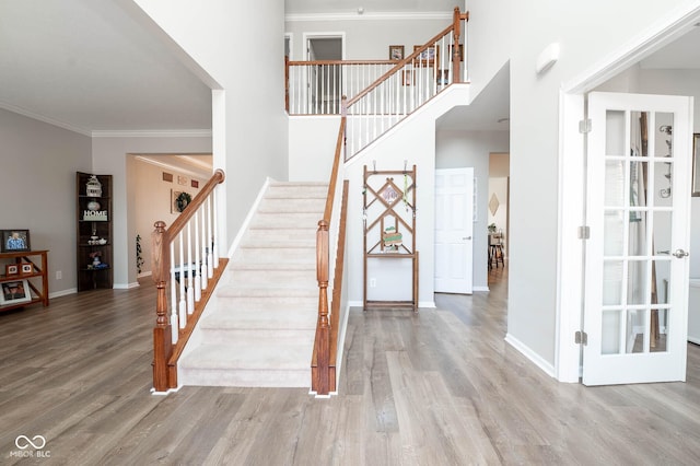 stairway featuring baseboards, a high ceiling, wood finished floors, and ornamental molding