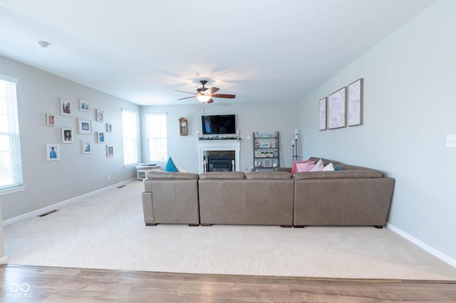 living area featuring visible vents, a glass covered fireplace, light wood-style floors, baseboards, and ceiling fan