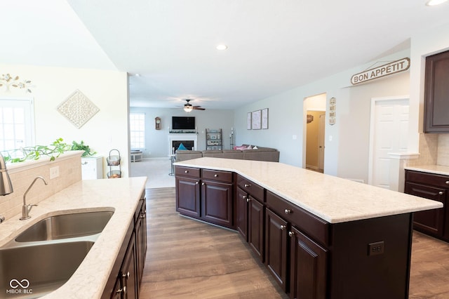 kitchen featuring backsplash, a kitchen island, a fireplace, a ceiling fan, and a sink