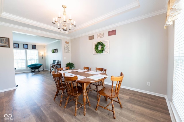 dining space with ornamental molding, a tray ceiling, wood finished floors, baseboards, and a chandelier