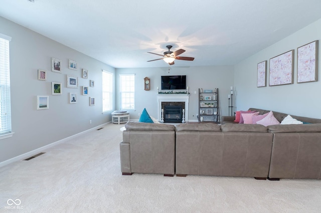 living area with visible vents, a ceiling fan, a glass covered fireplace, baseboards, and light colored carpet