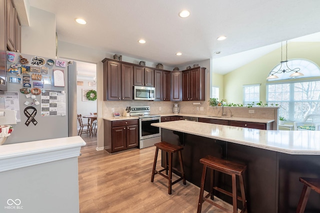 kitchen with a breakfast bar, a sink, stainless steel appliances, dark brown cabinets, and tasteful backsplash