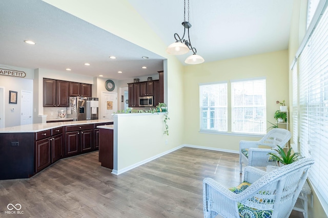 kitchen with wood finished floors, stainless steel appliances, hanging light fixtures, light countertops, and dark brown cabinets