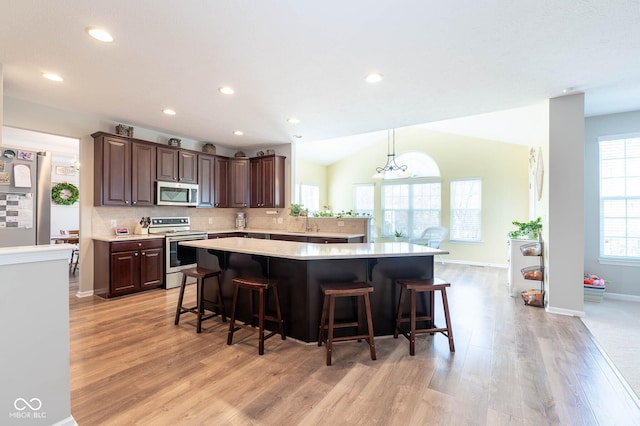 kitchen featuring backsplash, dark brown cabinetry, a breakfast bar area, light countertops, and stainless steel appliances