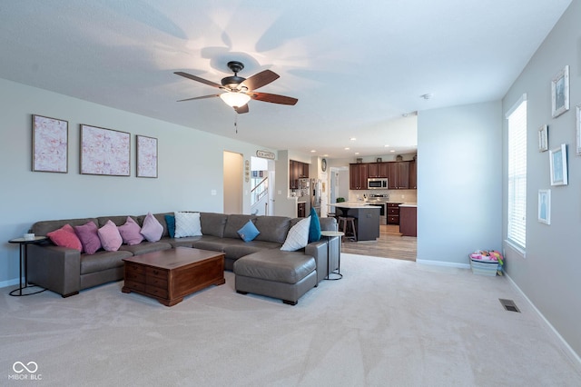 living area featuring light carpet, visible vents, baseboards, and ceiling fan