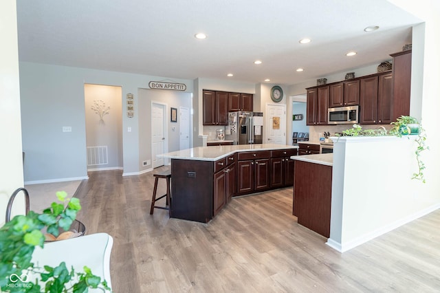 kitchen with visible vents, a kitchen island, dark brown cabinetry, a breakfast bar, and appliances with stainless steel finishes