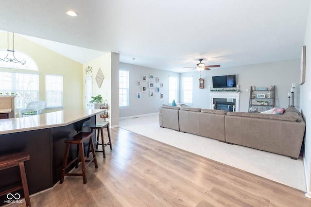 living area with wood finished floors, a ceiling fan, baseboards, lofted ceiling, and a glass covered fireplace