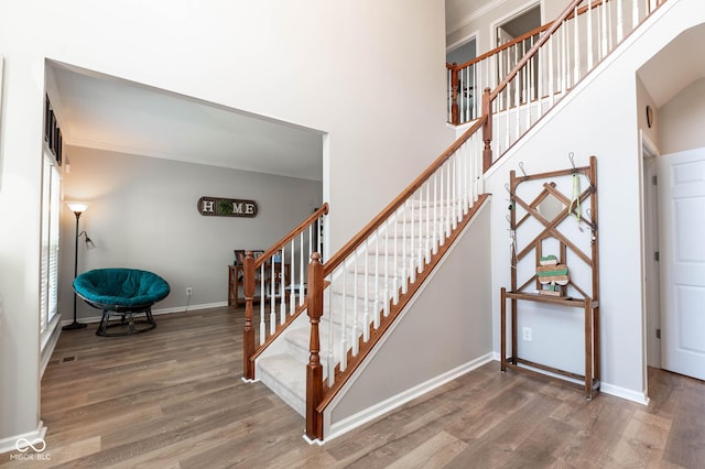 stairs featuring baseboards, a high ceiling, wood finished floors, and crown molding