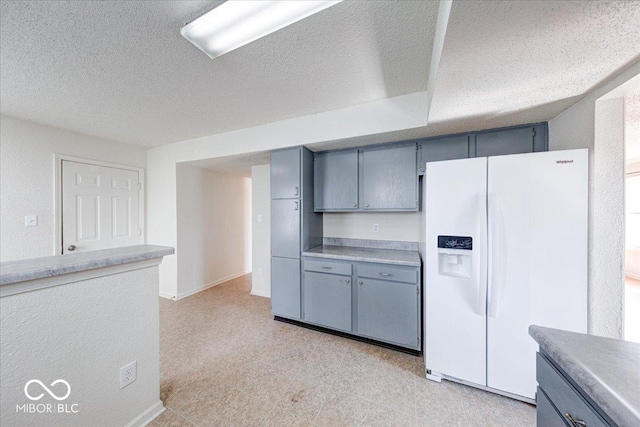 kitchen featuring a textured ceiling, white refrigerator with ice dispenser, gray cabinetry, and light countertops