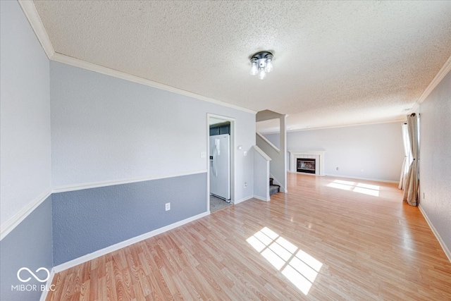 empty room with ornamental molding, a textured ceiling, wood finished floors, baseboards, and stairs