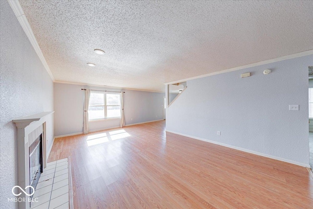 unfurnished living room featuring baseboards, a fireplace, ornamental molding, a textured wall, and light wood-type flooring