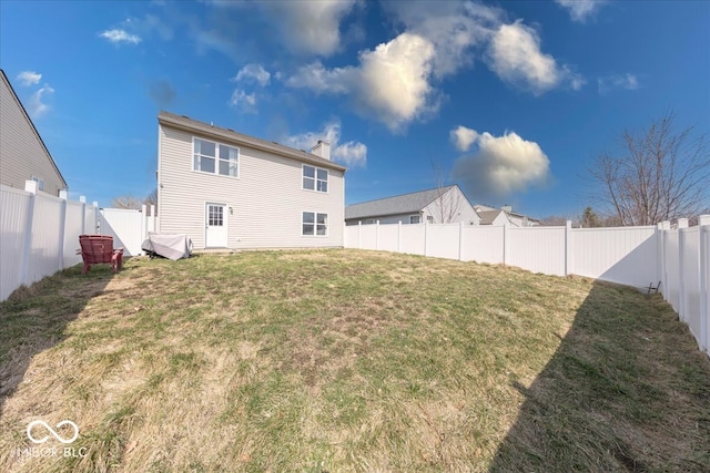 rear view of house with a fenced backyard, a chimney, and a yard