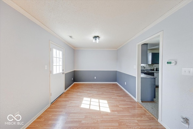 empty room featuring ornamental molding, light wood finished floors, and a textured ceiling