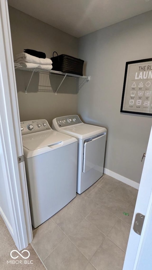 clothes washing area featuring baseboards, light tile patterned flooring, laundry area, and washing machine and clothes dryer