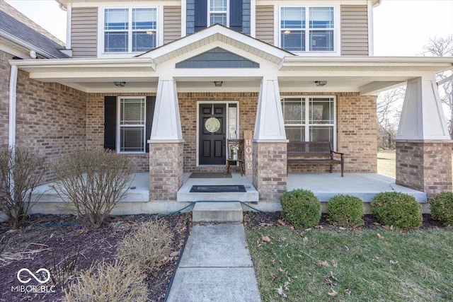 entrance to property featuring a porch and brick siding