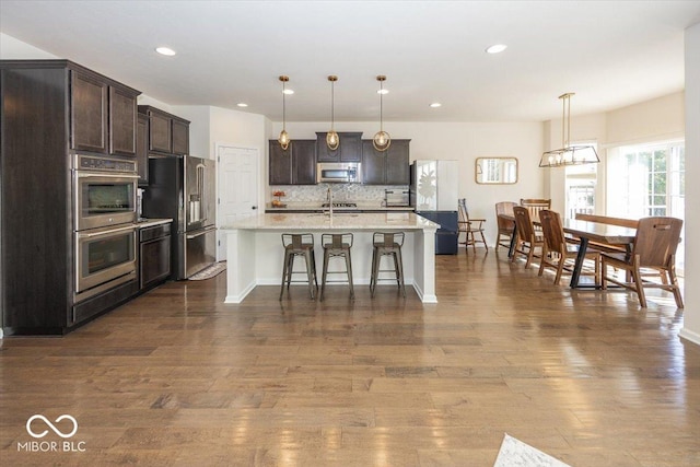 kitchen with tasteful backsplash, dark wood-style floors, appliances with stainless steel finishes, and a kitchen breakfast bar