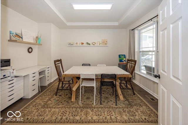 dining area featuring visible vents, a raised ceiling, baseboards, and dark wood-style flooring