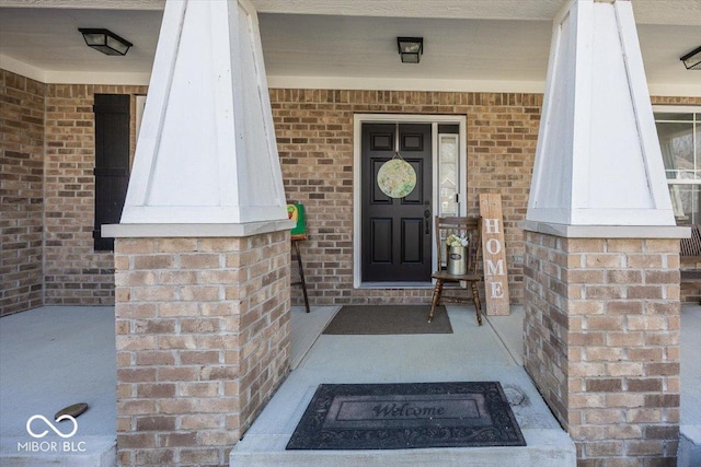 view of exterior entry featuring a porch and brick siding