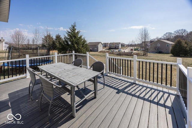 wooden terrace with outdoor dining area, a trampoline, a yard, and a residential view