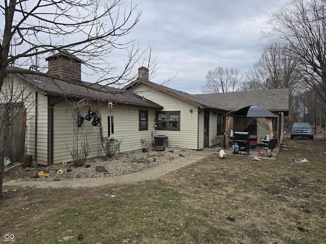 back of house with a gazebo, roof with shingles, central AC, and a chimney