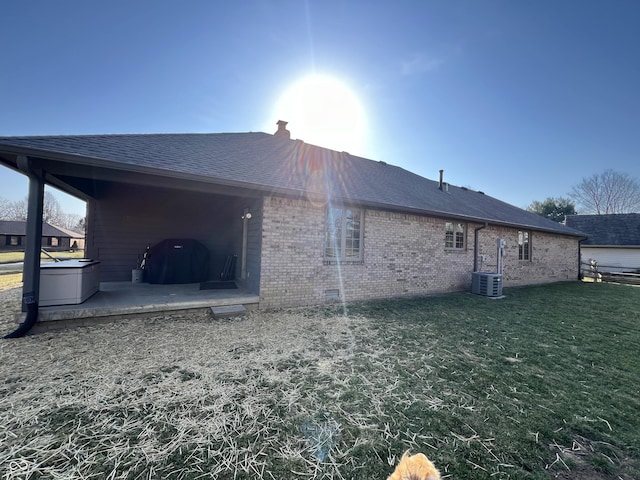 view of home's exterior with a lawn, a patio, a shingled roof, brick siding, and a chimney