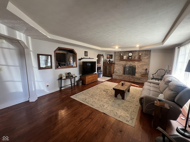 living room with dark wood-type flooring, a tray ceiling, a fireplace, arched walkways, and a textured ceiling