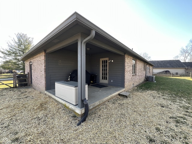 view of side of property featuring a patio, cooling unit, fence, a lawn, and brick siding