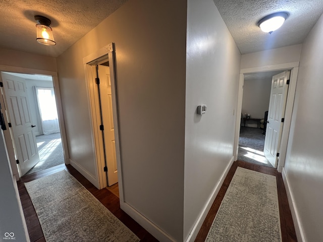 hallway with baseboards, dark wood-style flooring, and a textured ceiling