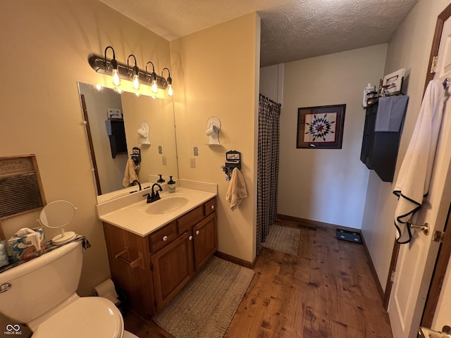 bathroom with baseboards, toilet, vanity, wood finished floors, and a textured ceiling