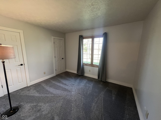 unfurnished bedroom with baseboards, dark colored carpet, and a textured ceiling