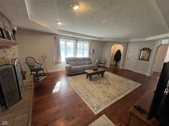 living room featuring a brick fireplace, baseboards, arched walkways, a textured ceiling, and dark wood-style flooring