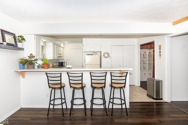 kitchen featuring a kitchen breakfast bar, freestanding refrigerator, a peninsula, white cabinets, and light countertops