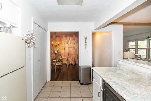 kitchen featuring wine cooler, light tile patterned floors, freestanding refrigerator, a textured ceiling, and white cabinetry