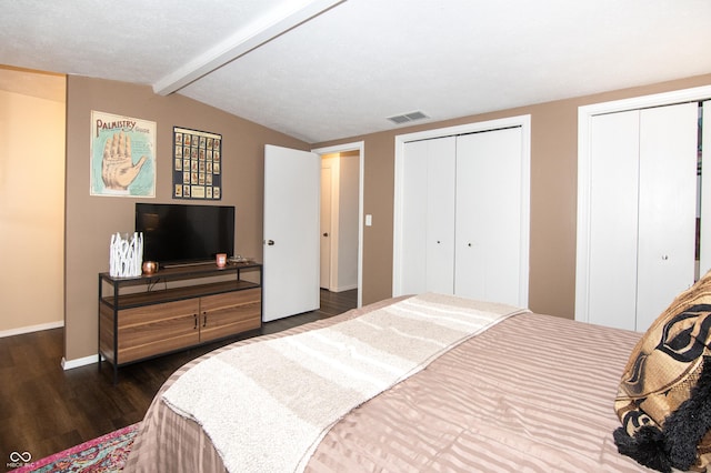 bedroom with visible vents, two closets, dark wood-style floors, baseboards, and vaulted ceiling with beams