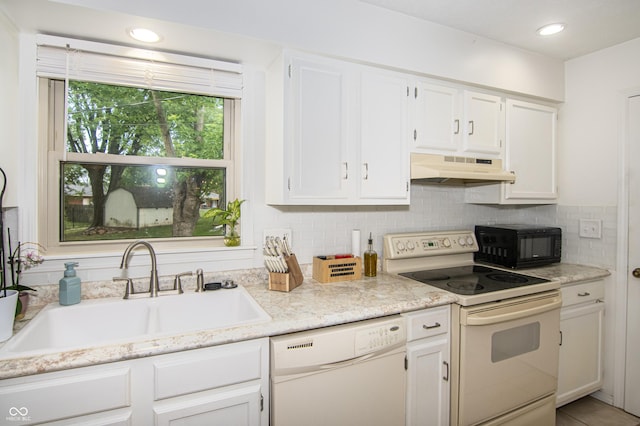 kitchen with under cabinet range hood, white appliances, white cabinetry, and a sink