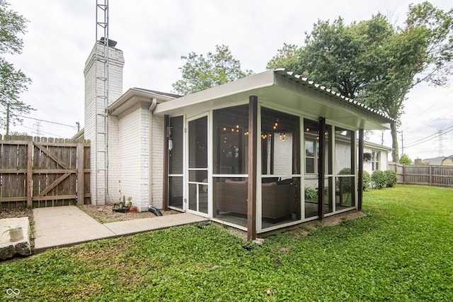 back of property featuring fence, a sunroom, a chimney, a lawn, and brick siding