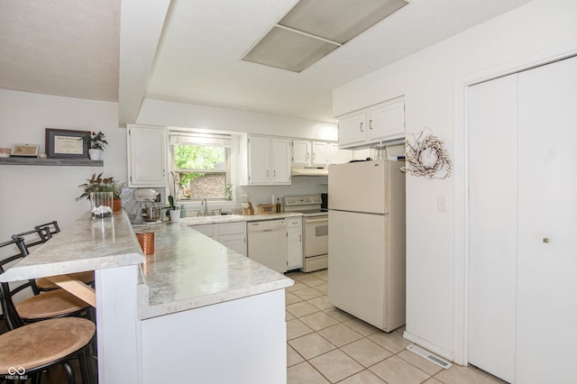 kitchen with under cabinet range hood, a breakfast bar, light countertops, a peninsula, and white appliances